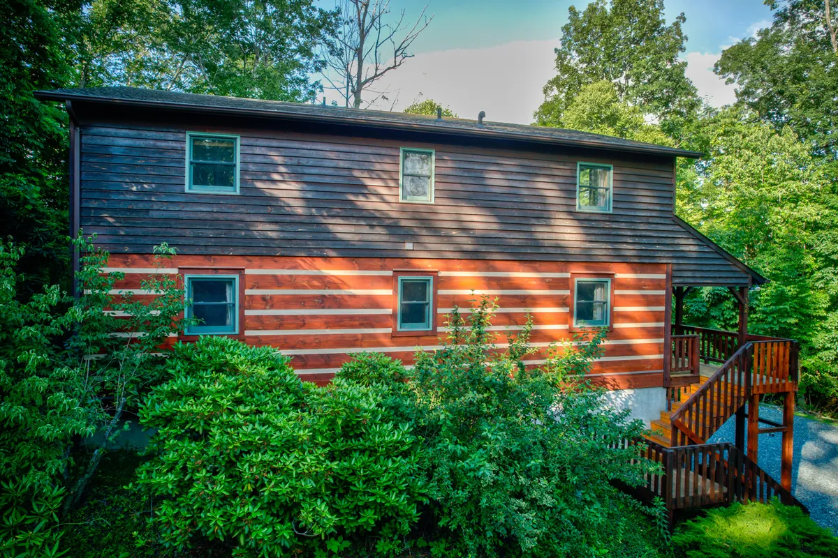 This exterior shot captures the inviting wooden siding of the lodge, large windows, and an accessible staircase leading to a cozy porch. The scene suggests a welcoming spot for guests to relax outdoors, framed by nature and hinting at the proximity to mountain trails and fresh air.