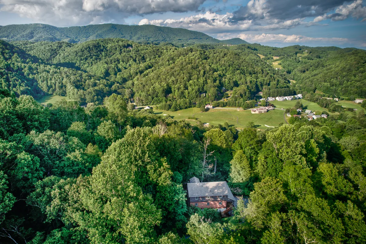 A breathtaking vista of layered mountain ranges, dense forests, and scattered homes, seen under a sky brushed with sunset hues. The panoramic view embodies the adventure and natural beauty accessible from the lodge, hinting at hiking, photography, and exploration opportunities.