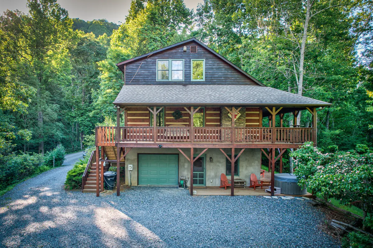 This exterior shot captures the welcoming front porch, a spacious wooden deck, large windows, and hints of the garage area. The deck is a prime spot for outdoor gatherings or simply soaking in the serene, natural surroundings.