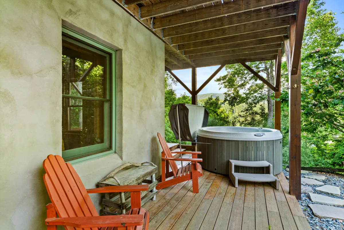 This image captures a wooden deck featuring a bubbling hot tub and vibrant red chairs, surrounded by lush greenery. The inviting setting suggests opportunities for relaxation, whether soaking in the hot tub or enjoying coffee on the deck while immersed in nature.