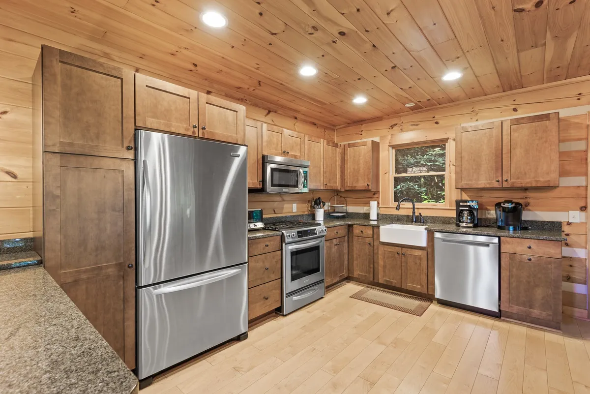 A bright, open kitchen featuring stainless steel KitchenAid appliances, granite countertops, and warm wooden cabinetry. A large window fills the space with natural light, highlighting the inviting, functional layout ideal for meal preparation and social gatherings.
