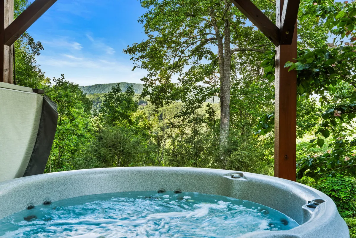 This exterior image features a bubbling hot tub nestled on a deck, surrounded by lush greenery and distant hills. The tranquil atmosphere is enhanced by the warm light of sunset, inviting guests to unwind while enjoying expansive outdoor views.
