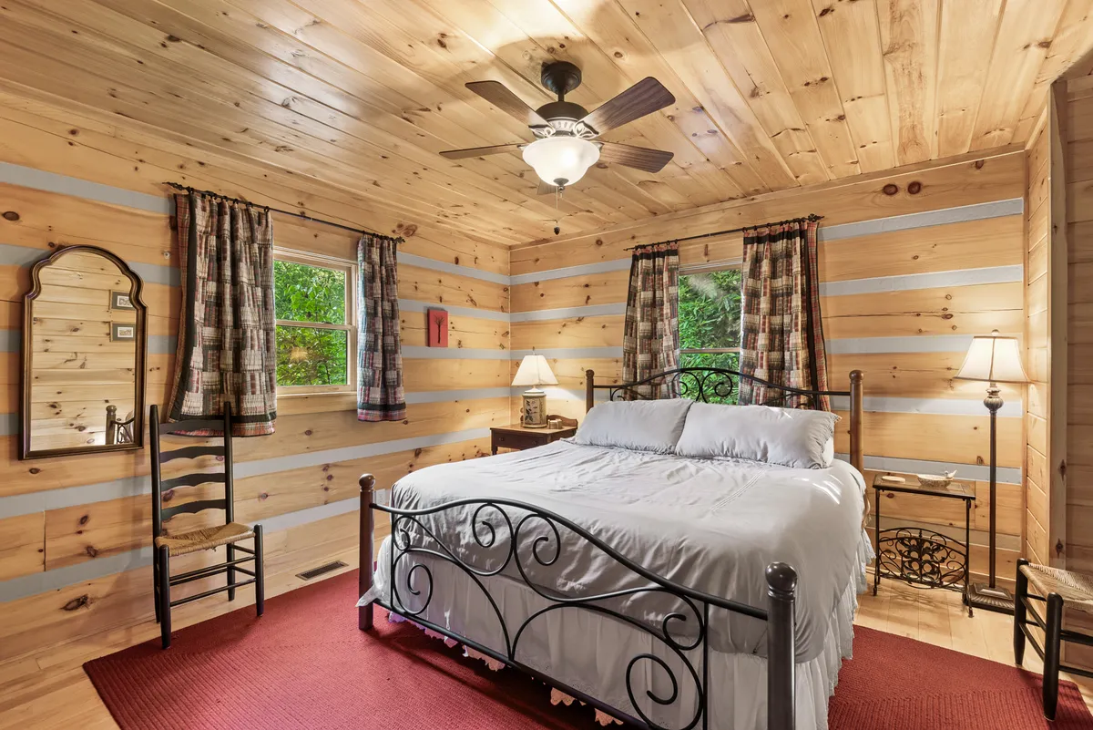 A tranquil bedroom with a large bed, soft linens, a comfortable chair, soft lighting from a window and lamp, and a mirror reflecting natural light. The space feels private and serene, with warm textures and neutral tones that invite restful sleep.