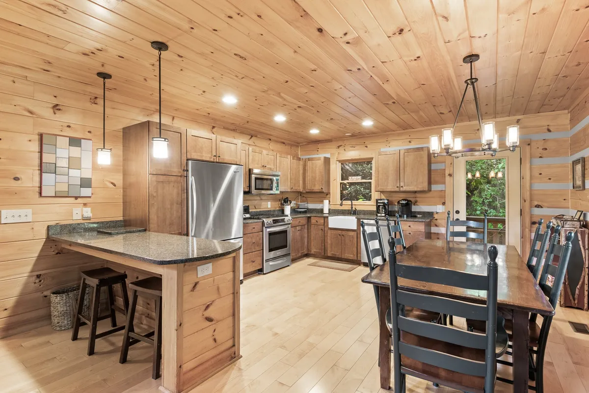 An inviting angle of the open living space reveals a kitchen island, an extended wooden dining table, and stainless steel appliances. The seamless flow between kitchen and dining areas evokes a sense of togetherness and celebration.