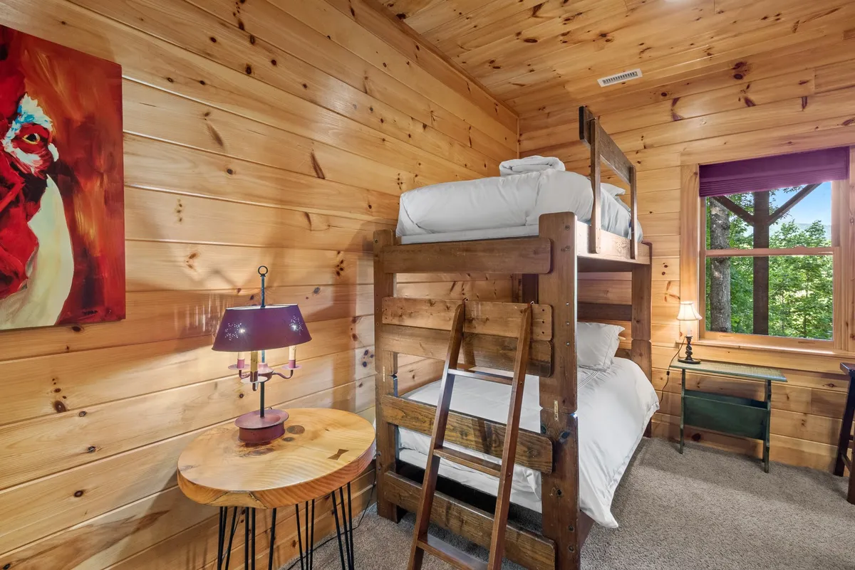 A playful and inviting bunk bed bedroom with vibrant artwork, a cozy lamp, and a window offering views of the outdoors. The space is designed for fun sleepovers or peaceful retreats, with soft bedding and personal touches.