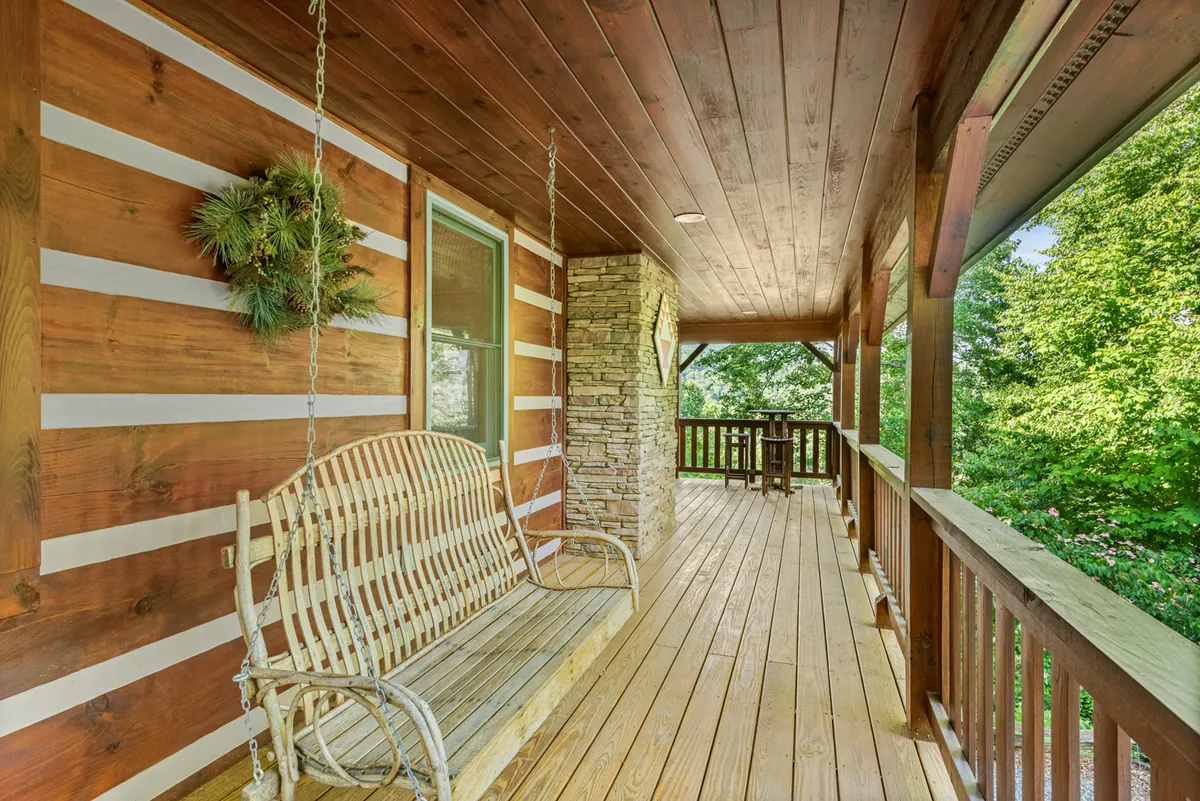 An inviting porch scene with a swing bench, wooden railing, stone pillars, and flourishing greenery in the background. The tranquil atmosphere is ideal for sipping morning coffee, reading, or enjoying the sounds of nature with friends.