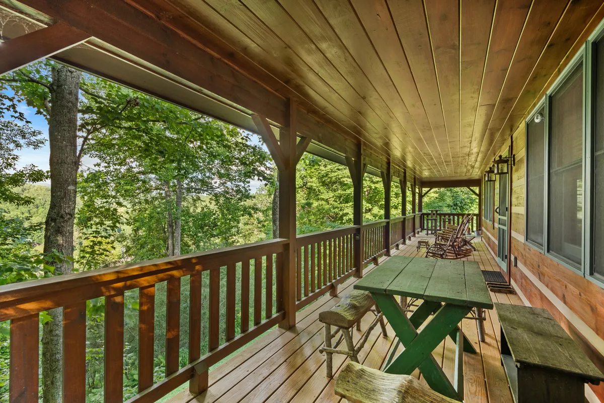 A tranquil wooden deck scene featuring a green table, rocking chairs, and surrounding trees. This space is ideal for outdoor dining, relaxing, or having a quiet family moment amidst nature.