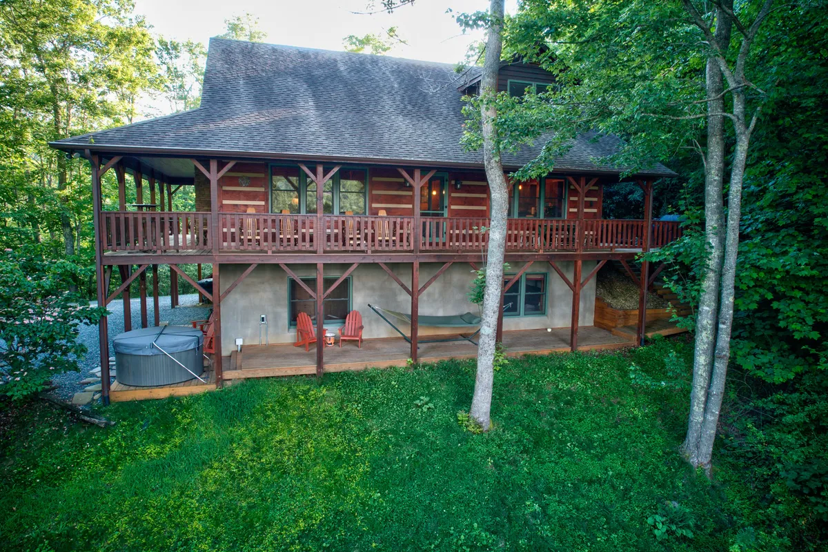 A tranquil wooden deck is furnished with red Adirondack chairs and a hammock, with greenery all around. The setup invites both solitude and togetherness, ideal for enjoying sunsets, relaxing with a book, or swaying gently in the hammock.