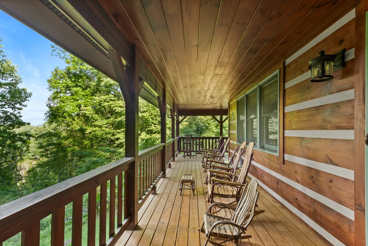 A peaceful porch scene featuring classic rocking chairs and a sturdy wooden railing, surrounded by lush greenery. The vantage point hints at the tranquility available after a day of exploration, offering a spot for guests to soak up nature, watch sunsets, or gather with others.