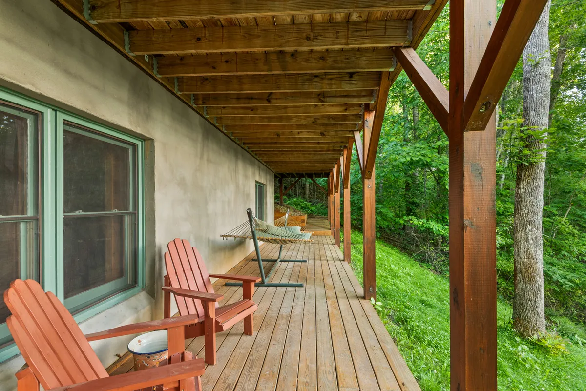 This exterior image showcases a spacious wooden deck outfitted with red Adirondack chairs and a hammock, set against a lush green backdrop. The scene captures the essence of outdoor relaxation and socializing, with ample seating for group gatherings and tranquil views of the surrounding nature.