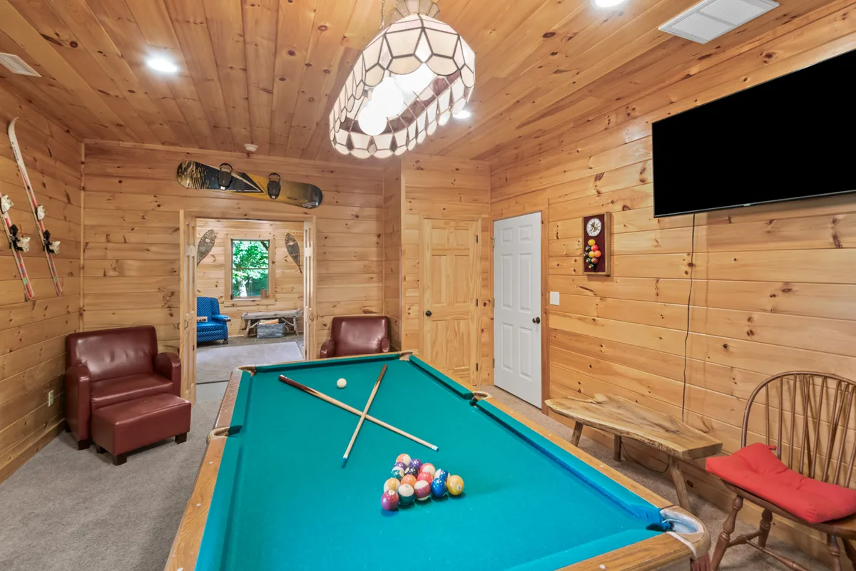 A cozy interior recreation space featuring a pool table, plush leather chairs, wooden walls, and distinctive lighting. The arrangement encourages casual hangouts, friendly billiards matches, and relaxed socializing.