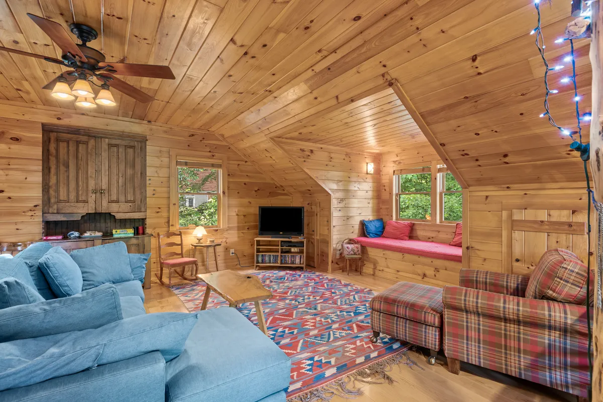This warm, inviting lounge area boasts a plaid armchair, a comfortable sectional sofa, a colorful area rug, a wooden ceiling, and a well-placed TV unit. The natural light and abundance of seating provide the perfect setting for movie nights or board games.